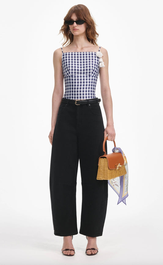 Woman wearing a checkered top and black pants, holding a brown handbag with a white background
