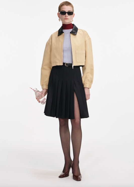 Woman wearing a beige jacket, black skirt, and sunglasses on a white background