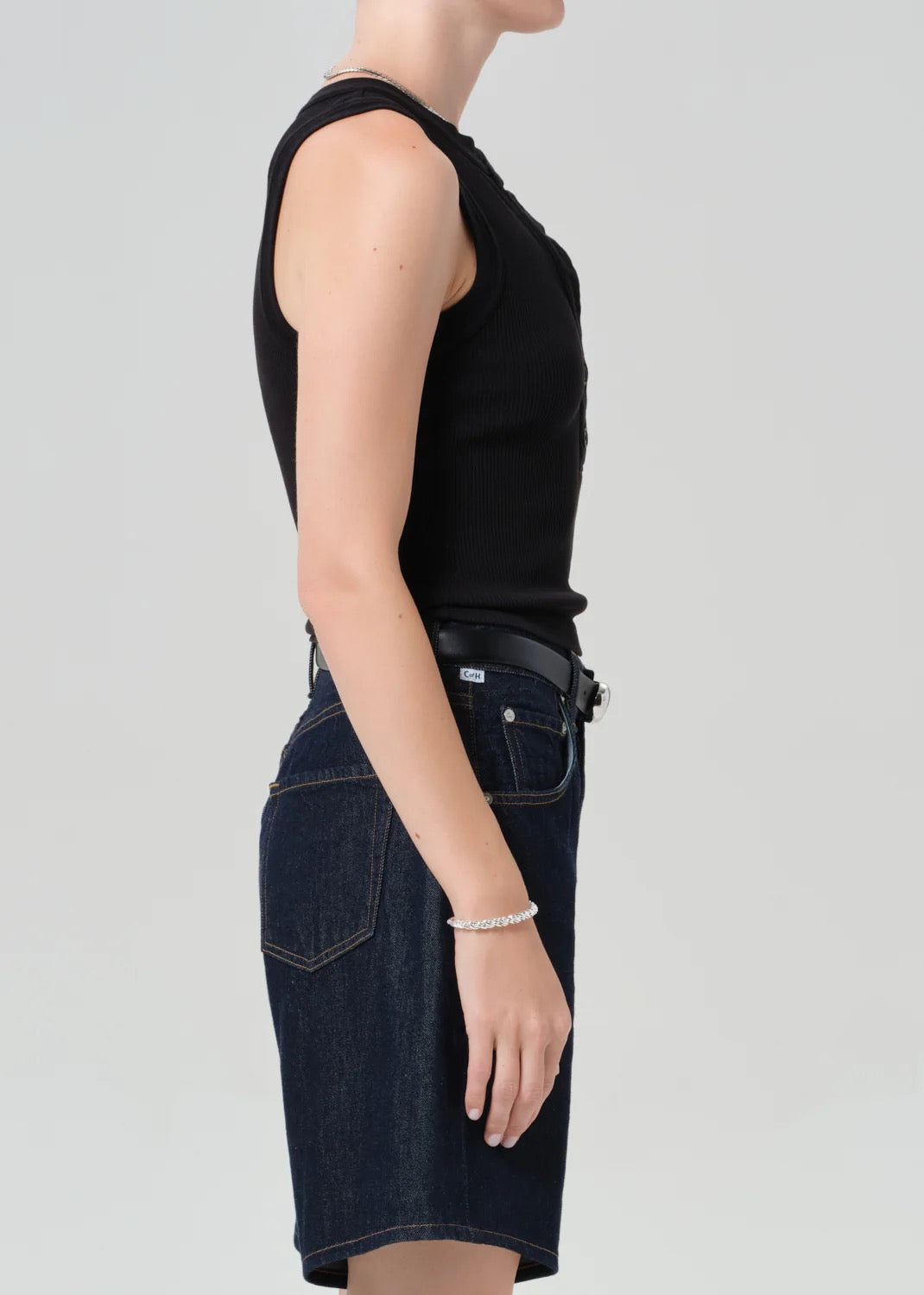 Person wearing a black sleeveless top and dark denim skirt on a light gray background