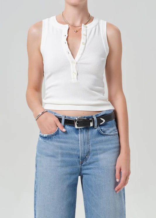 Person wearing a white sleeveless top and blue jeans on a plain background