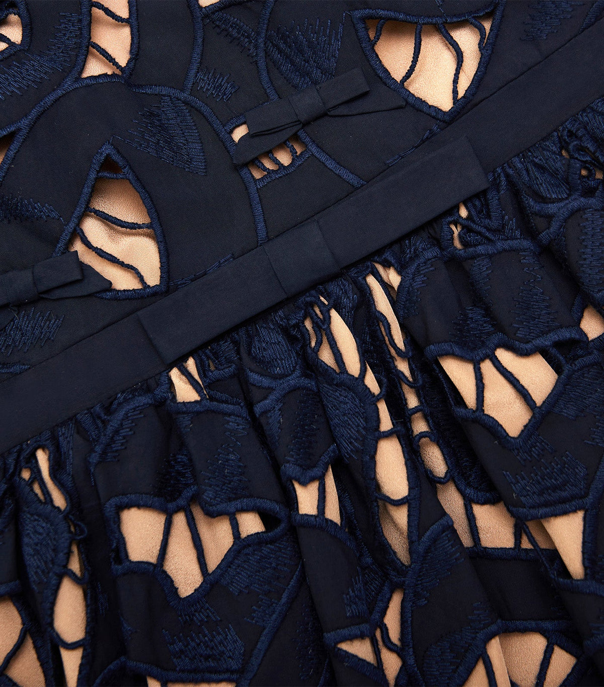 Close-up of the bow appliqués, waistband and openwork embroidery on the navy mini dress
